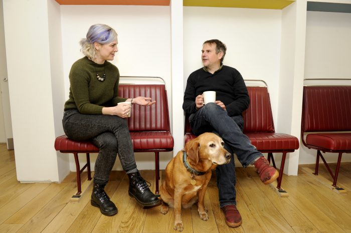 Man and woman chatting in a coworking space with dog at their feet.